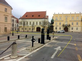 A street intersection with a statue, bollards, and buildings with classical architecture.