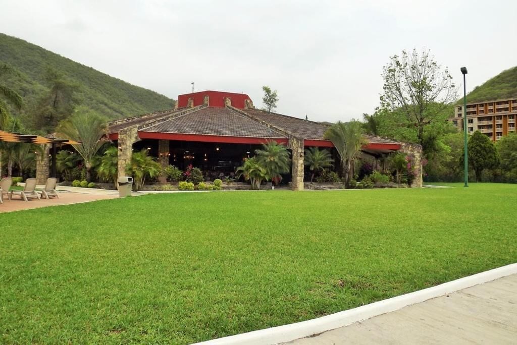 A building with a red roof and stone walls, surrounded by a well-maintained lawn and palm trees.