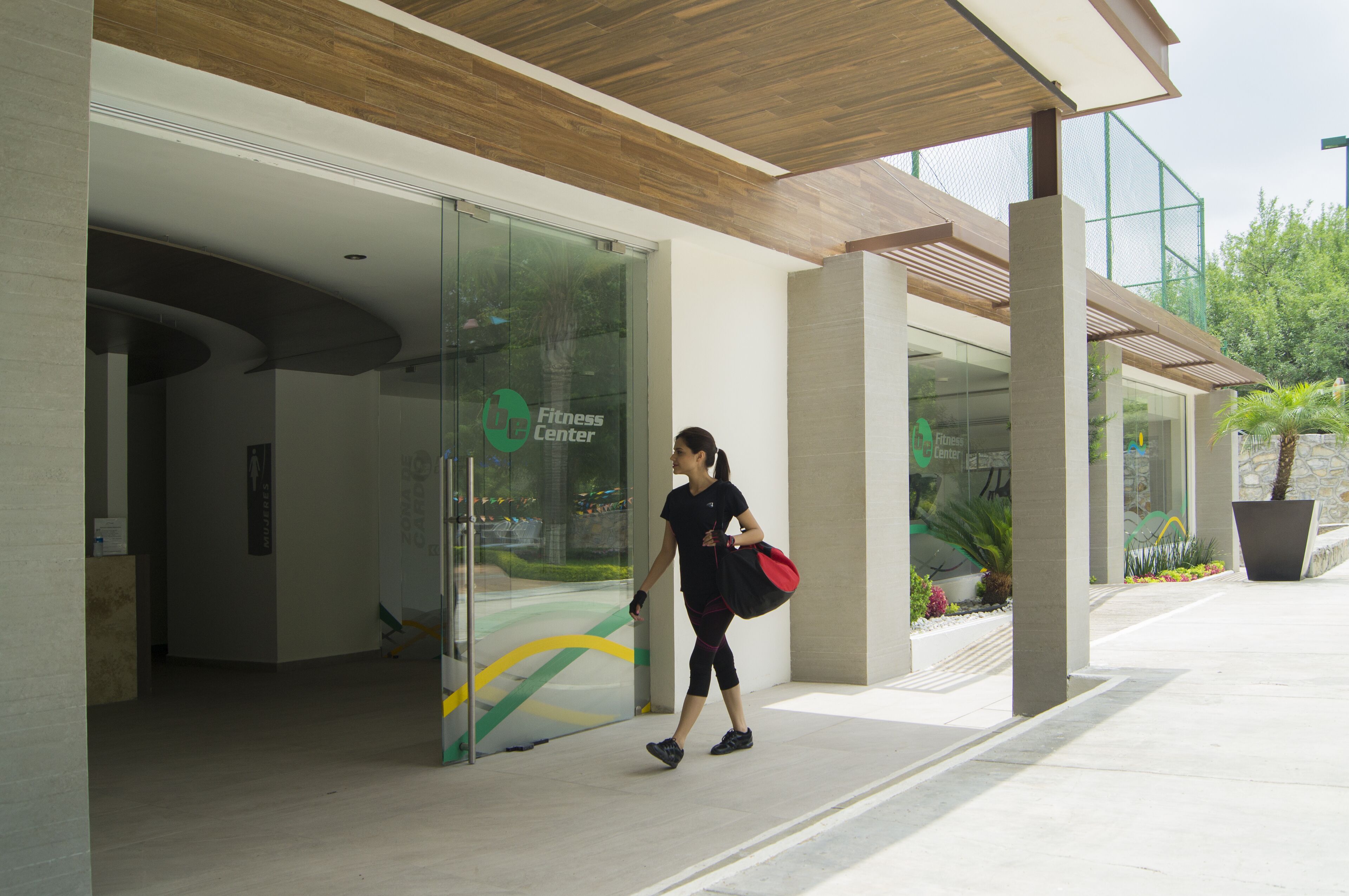 Une femme se dirige vers un bâtiment dont l’entrée est en verre et sur laquelle on peut lire l’inscription « Centre de remise en forme ».