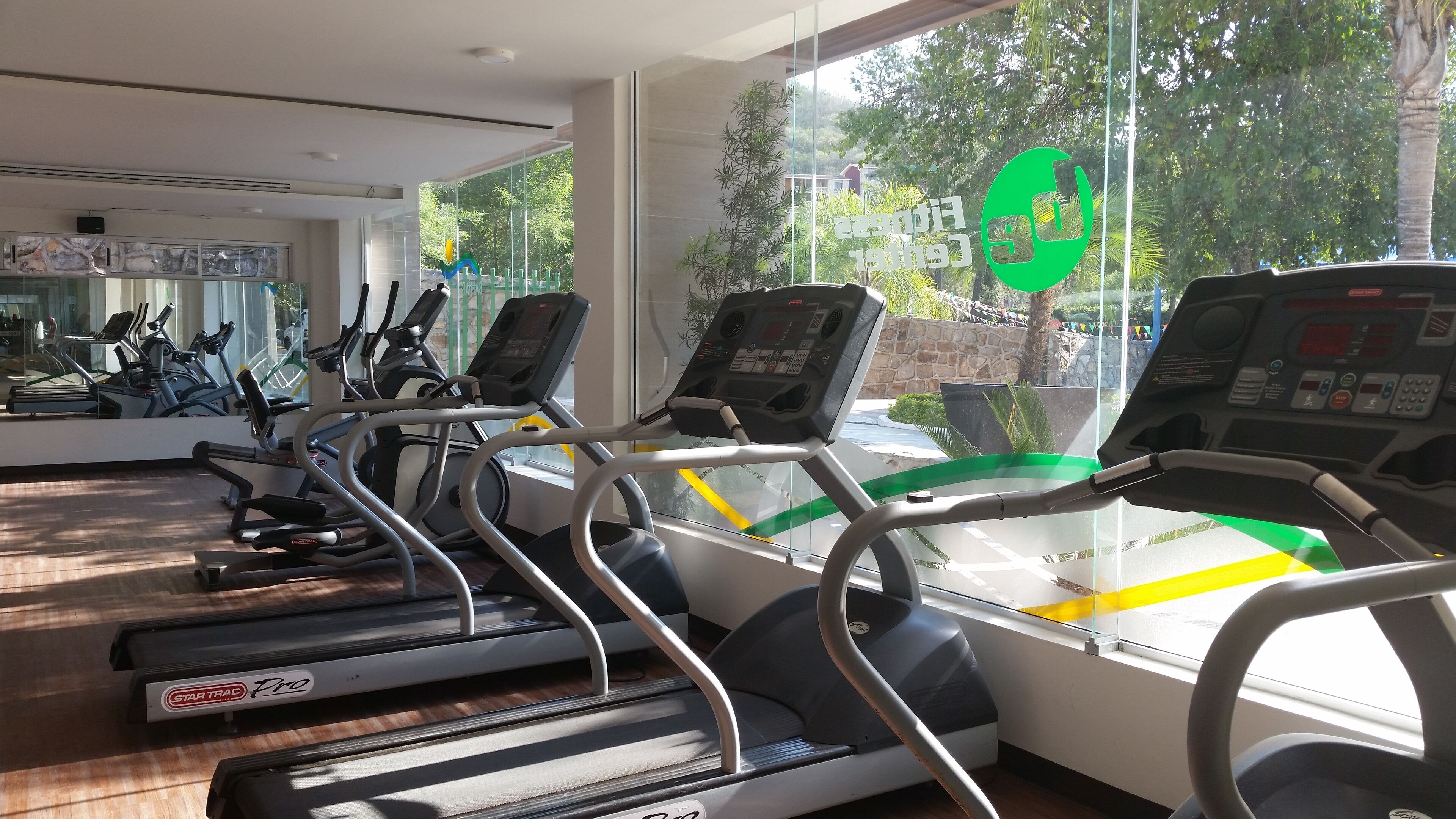 Un gimnasio con cintas de correr, bicicletas estáticas y un espejo grande.