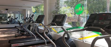 Un gimnasio con cintas de correr, bicicletas estáticas y un espejo grande.