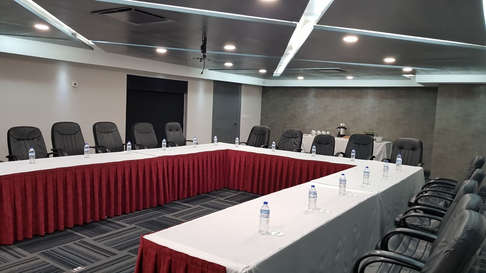 Un salón de conferencias con dos mesas largas, cada una cubierta con un mantel rojo y equipadas con botellas de agua.
