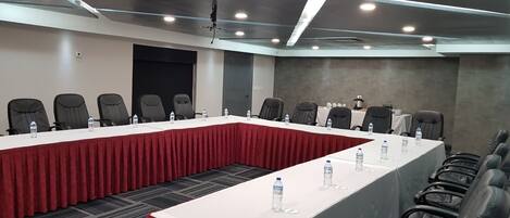 Un salón de conferencias con dos mesas largas, cada una cubierta con un mantel rojo y equipadas con botellas de agua.