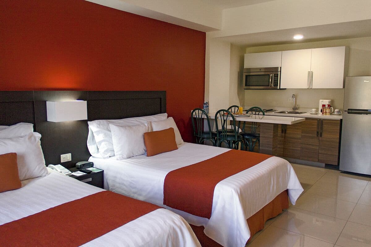 Habitación de hotel con dos camas, kitchenette y comedor.