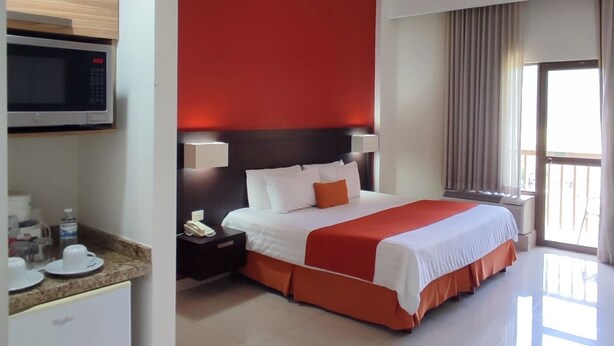 A hotel room with a bed, a microwave, a refrigerator, and a window with curtains. - Bahía Escondida (Santiago)