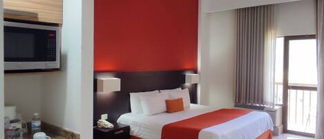 Habitación de hotel con cama, microondas, refrigerador y ventana con cortinas.