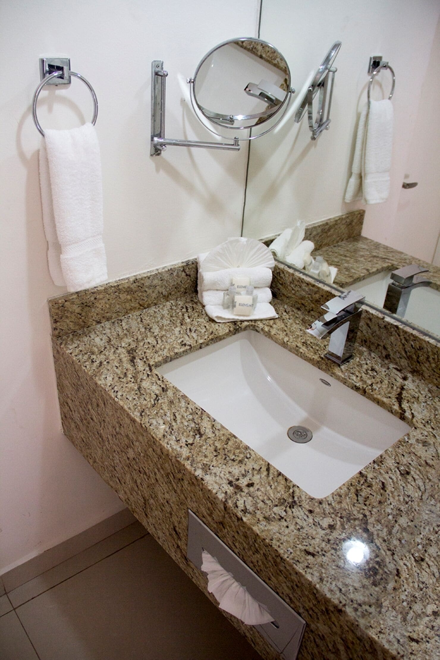 Une salle de bain avec un comptoir en granit, un lavabo blanc, un miroir et deux porte-serviettes.