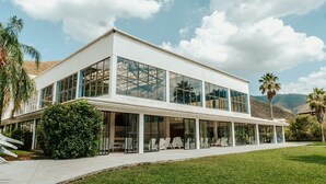 A modern two-story building with large glass windows, a flat roof, and a covered patio area with outdoor seating.