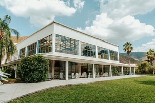 Un edificio moderno de dos pisos con amplios ventanales de vidrio, techo plano y un patio cubierto con asientos al aire libre.
