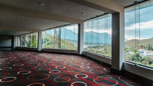 A spacious room with large windows offering a mountain view. The room has a patterned carpet and a modern ceiling.