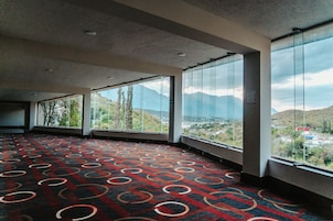 Amplia habitación con grandes ventanales que ofrecen vistas a la montaña. La habitación tiene una alfombra estampada y un techo moderno.