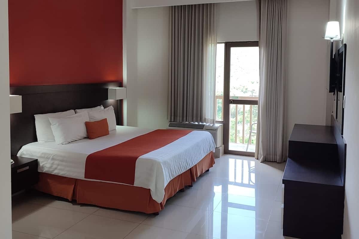 Una habitación de hotel moderna con una cama grande, un televisor de pantalla plana y un balcón con cortinas.