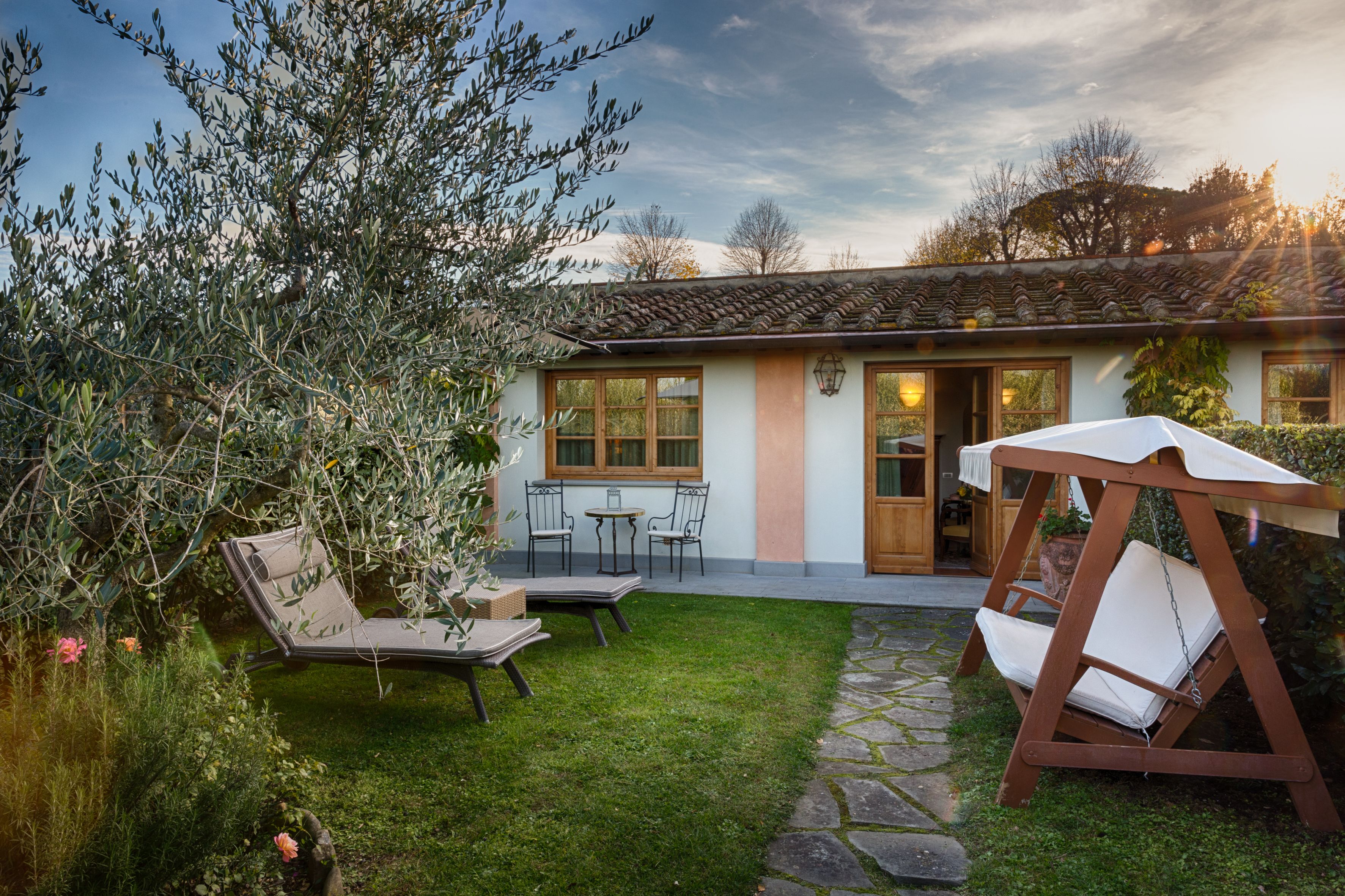 A house with a garden, a swing chair, and a table with chairs.