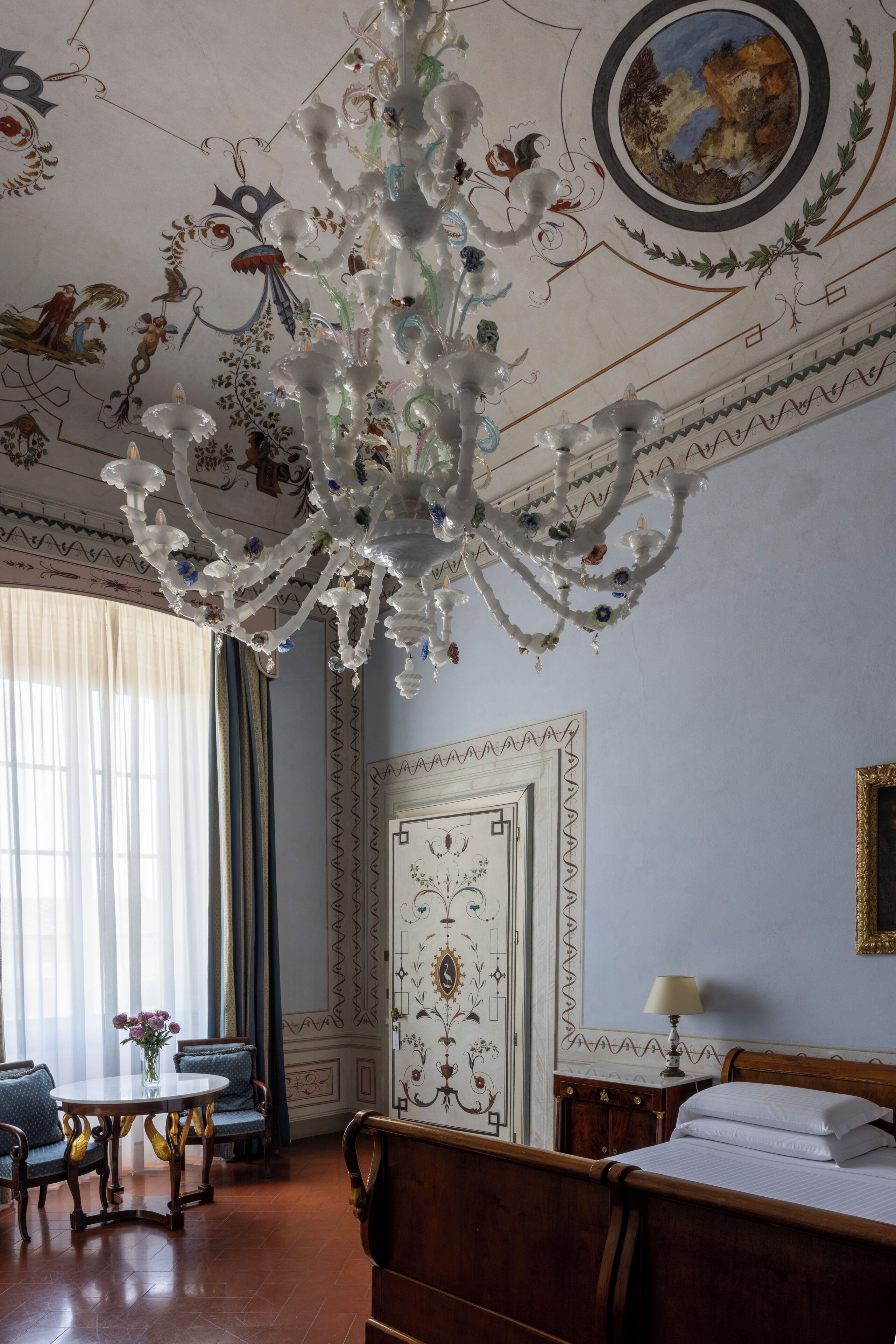 Una habitación con candelabro, cama, mesa y silla.