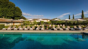 A swimming pool with lounge chairs and umbrellas, surrounded by greenery and buildings. - Villa Olmi Firenze (Bagno a Ripoli)