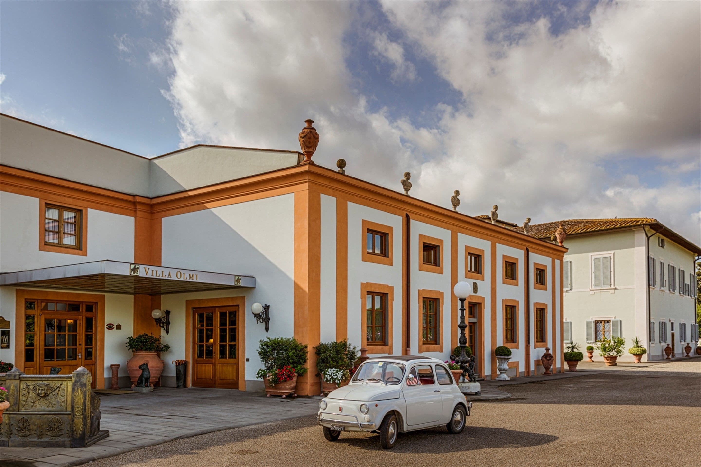 A villa with a classic architectural style, featuring a central entrance with a canopy, multiple windows, and a small car parked in front.
