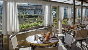 Un espacio exterior con mesas y sillas para comer, vistas a un jardín y un edificio al fondo.