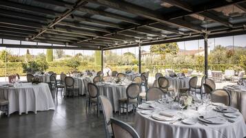 Un espace de restauration en plein air avec des tables rondes dressées pour un événement formel, entourées de chaises, et offrant une vue sur un jardin aménagé.