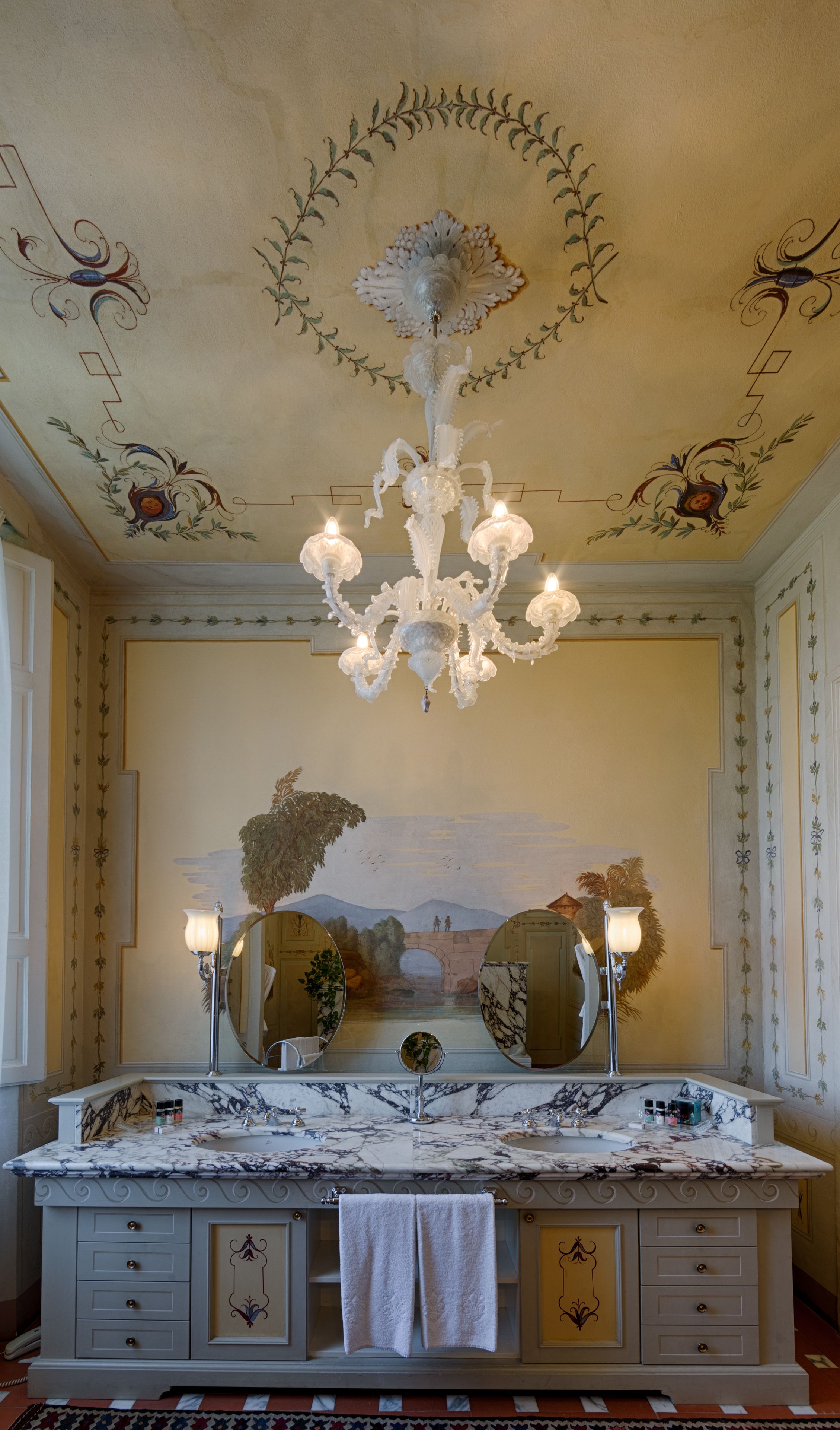 A luxurious bathroom with a marble vanity, a large mirror, and a decorative chandelier.