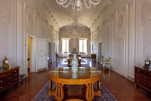A grand room with a large round table, ornate chandeliers, and classical architecture.