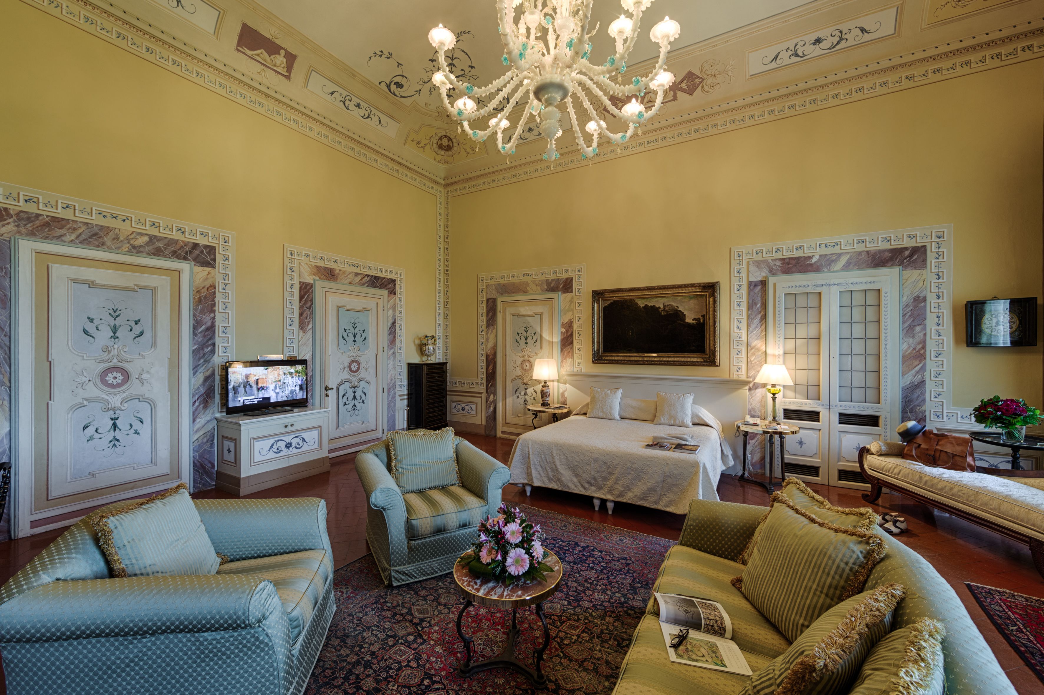 A spacious room with a large bed, a television, and a chandelier.