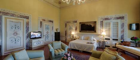 Una habitación amplia con una cama grande, televisión y candelabro.
