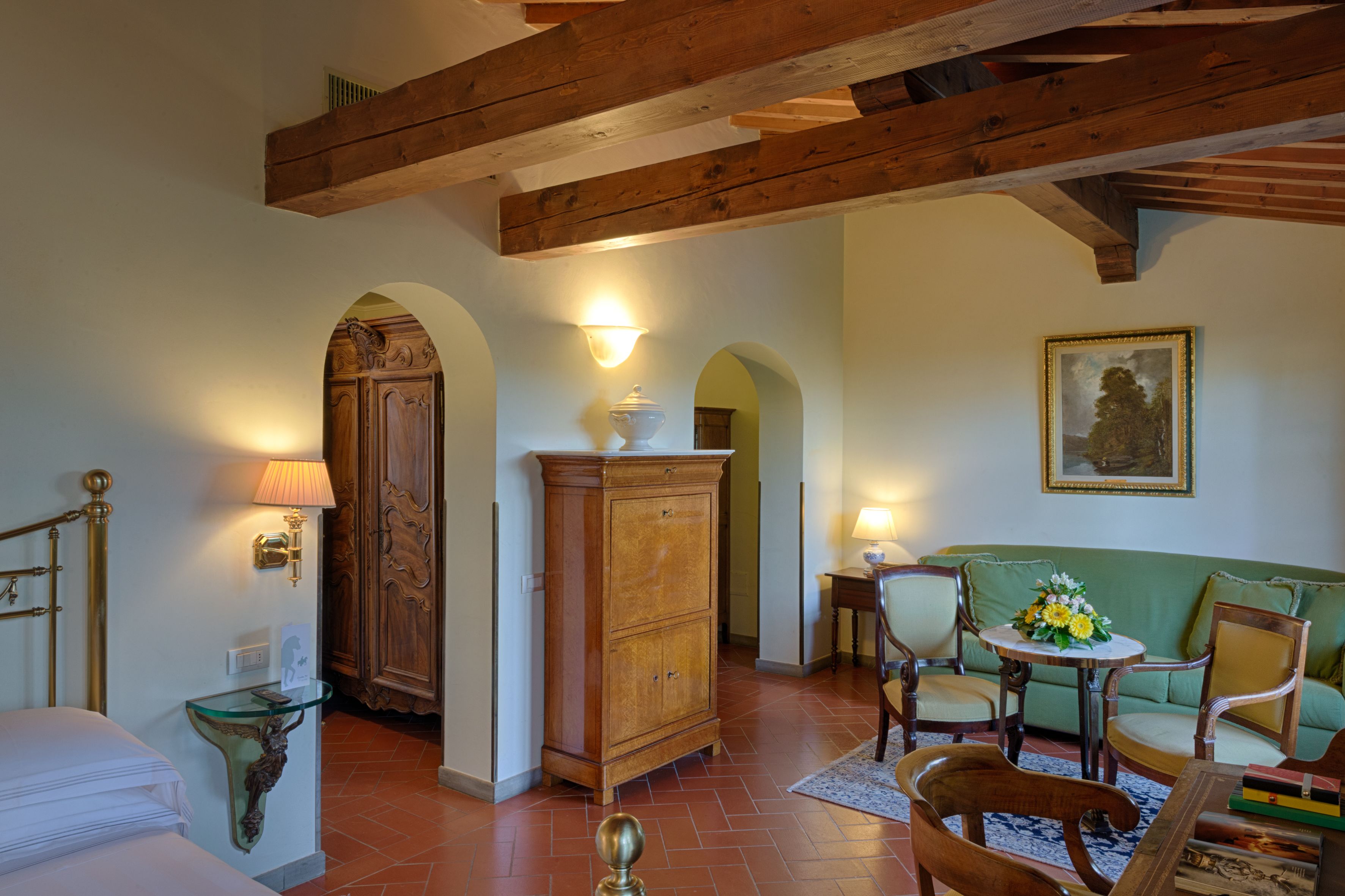A room with a wooden cabinet, a green sofa, a dining table with chairs, and a painting on the wall.