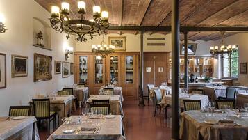 A restaurant with multiple dining tables set for guests, wooden cabinets with wine bottles, and a brick ceiling.