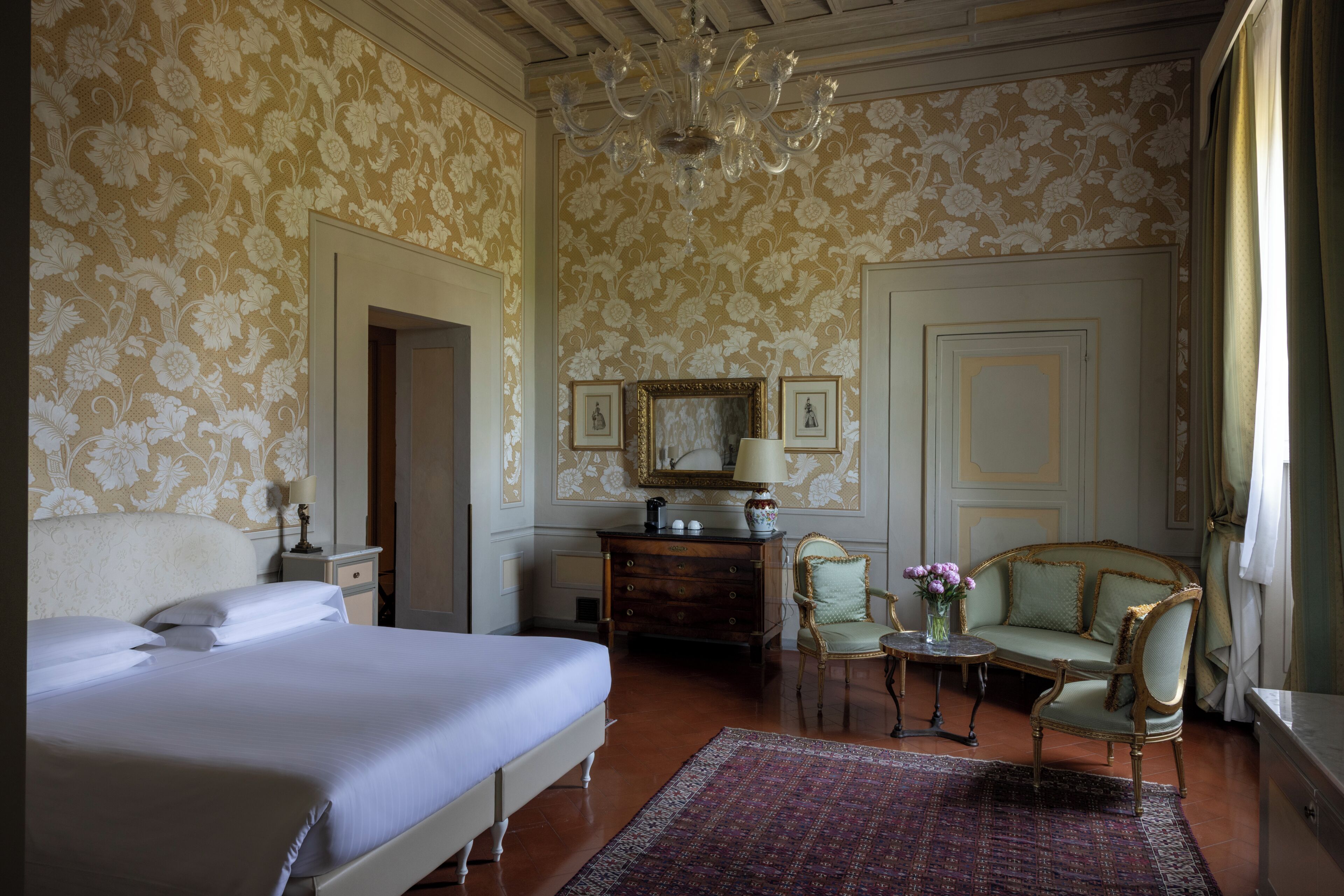 Ein Schlafzimmer mit einem großen Bett, einem Schminktisch, einem Stuhl, einem kleinen Tisch mit einer Vase und einer Kandelaber.