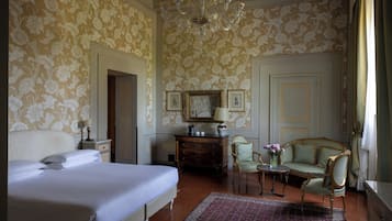 Ein Schlafzimmer mit einem großen Bett, einem Schminktisch, einem Stuhl, einem kleinen Tisch mit einer Vase und einer Kandelaber.