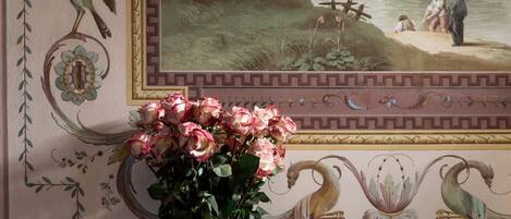 Een kamer met een muurschildering van een vredig landschap, een vaas met roze rozen en decoratieve muurpatronen.