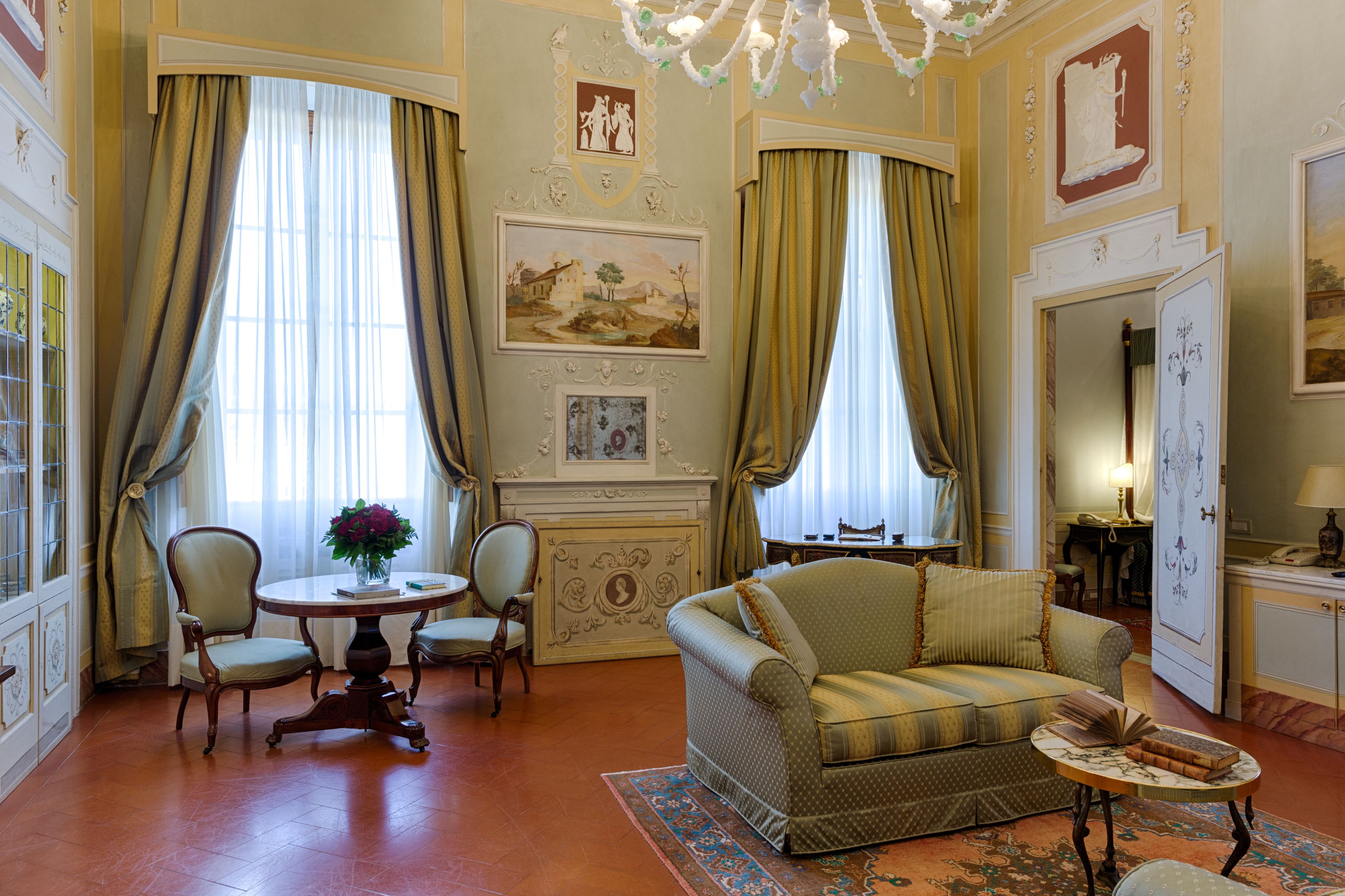 A room with a sofa, chairs, a table with a vase, and a fireplace.