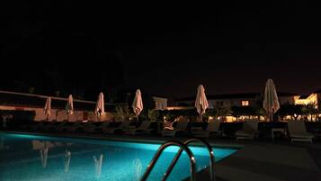 Zona de piscina nocturna con sillones de descanso y sombrillas.