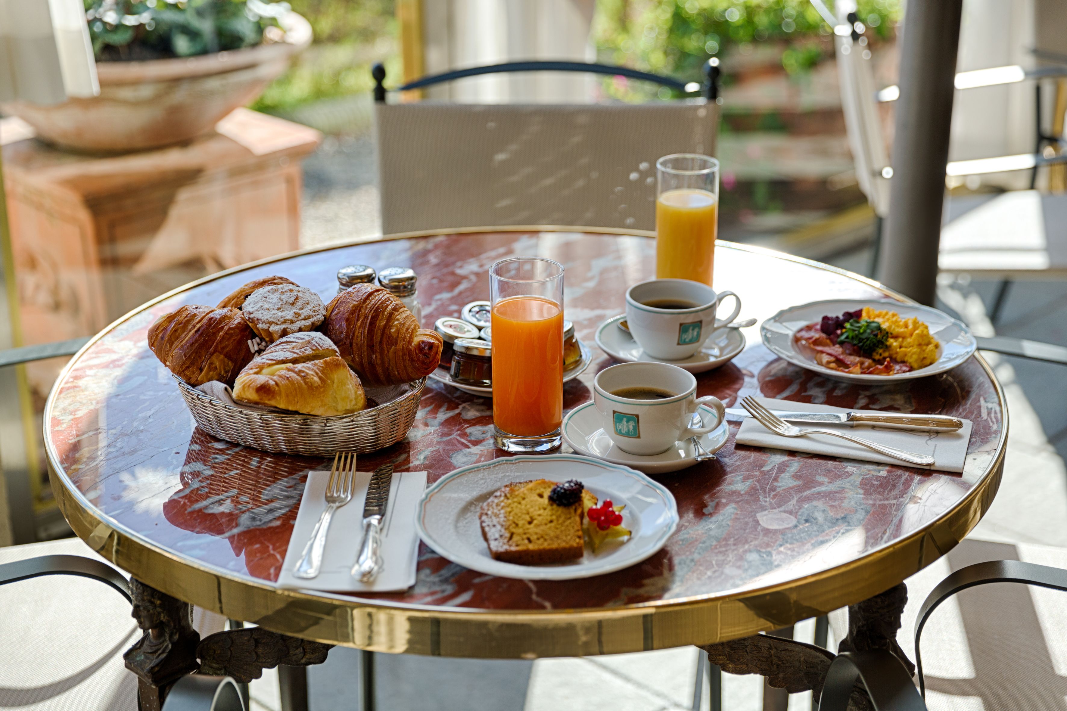 Una mesa de desayuno con croissants, jugo, café y un plato de comida.
