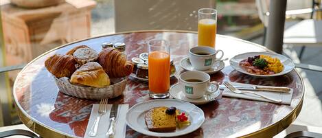 A breakfast table with croissants, juice, coffee, and a plate of food.