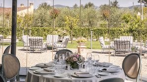 An outdoor dining area with tables set for a meal, surrounded by chairs and a garden view. - Villa Olmi Firenze (Bagno a Ripoli)
