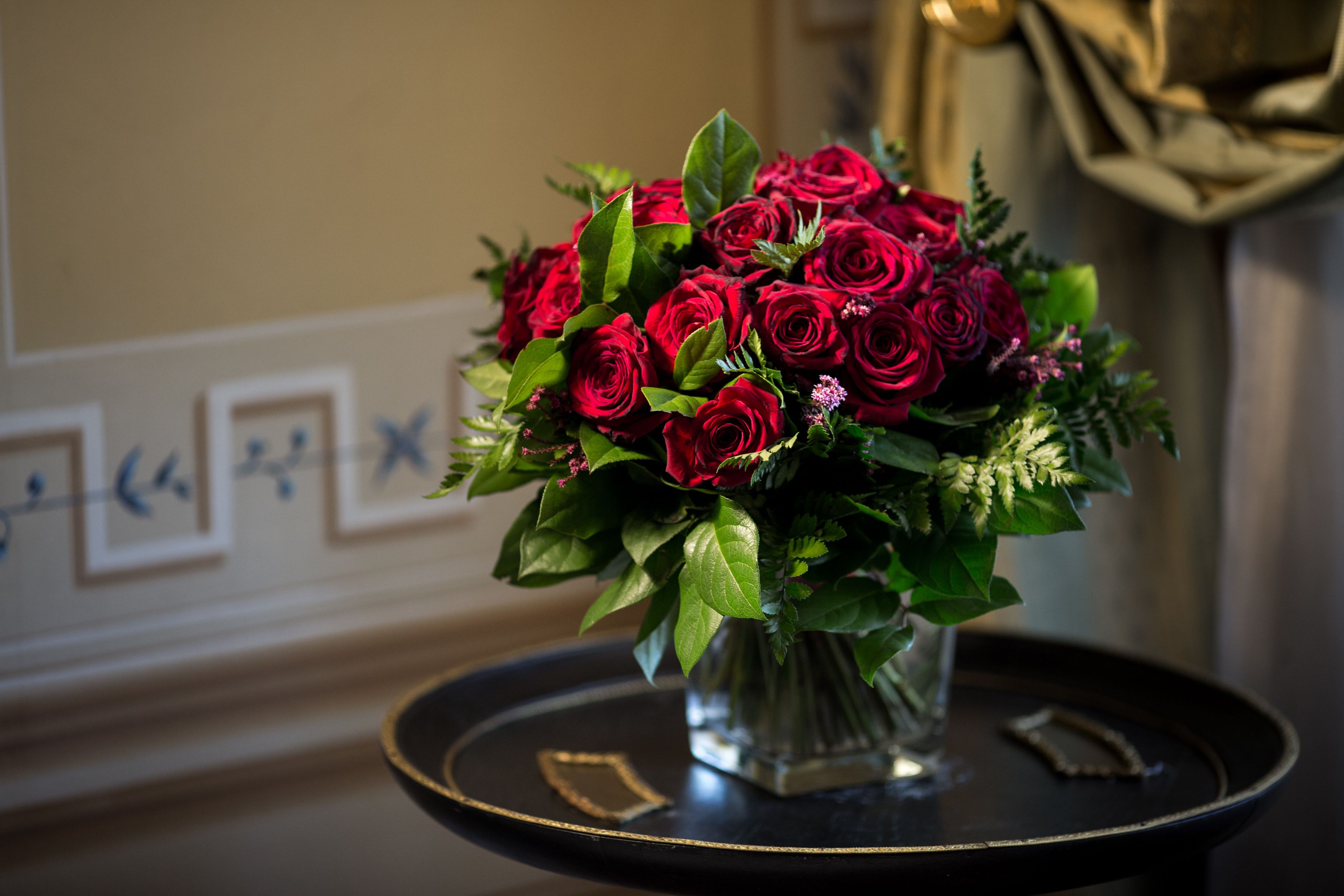 A bouquet of red roses in a clear glass vase on a black tray with gold trim.