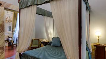 Una cama con dosel y cuatro columnas, con un edredón estampado, una mesita de noche con lámpara y una silla en una habitación con paredes de mármol y una puerta decorada con un cuadro.