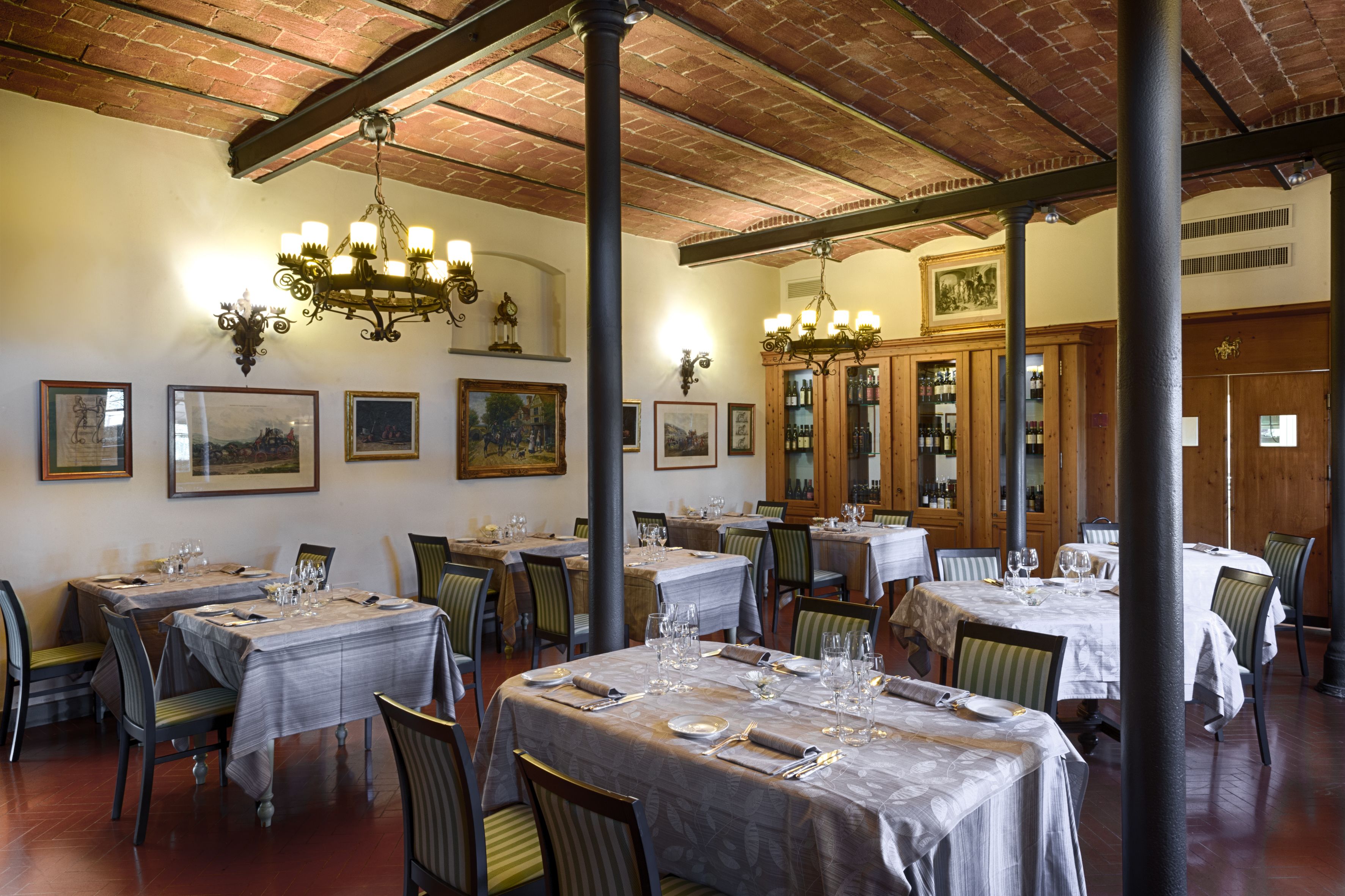 A restaurant with multiple tables set for dining, wooden chairs, and a chandelier.