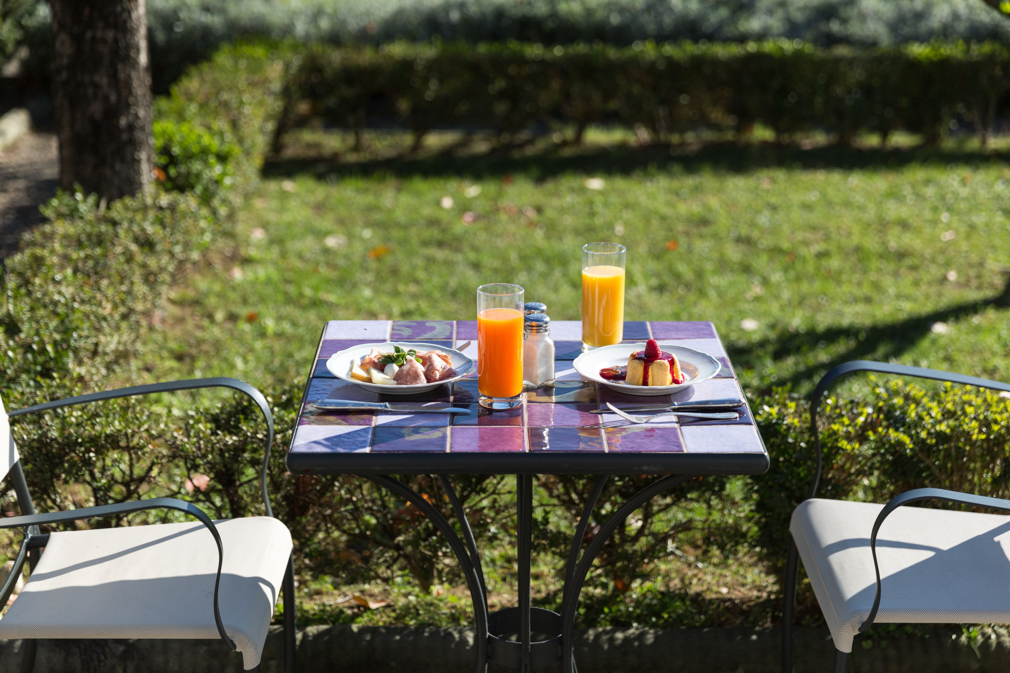 An outdoor dining table with plates of food and drinks, surrounded by chairs.
