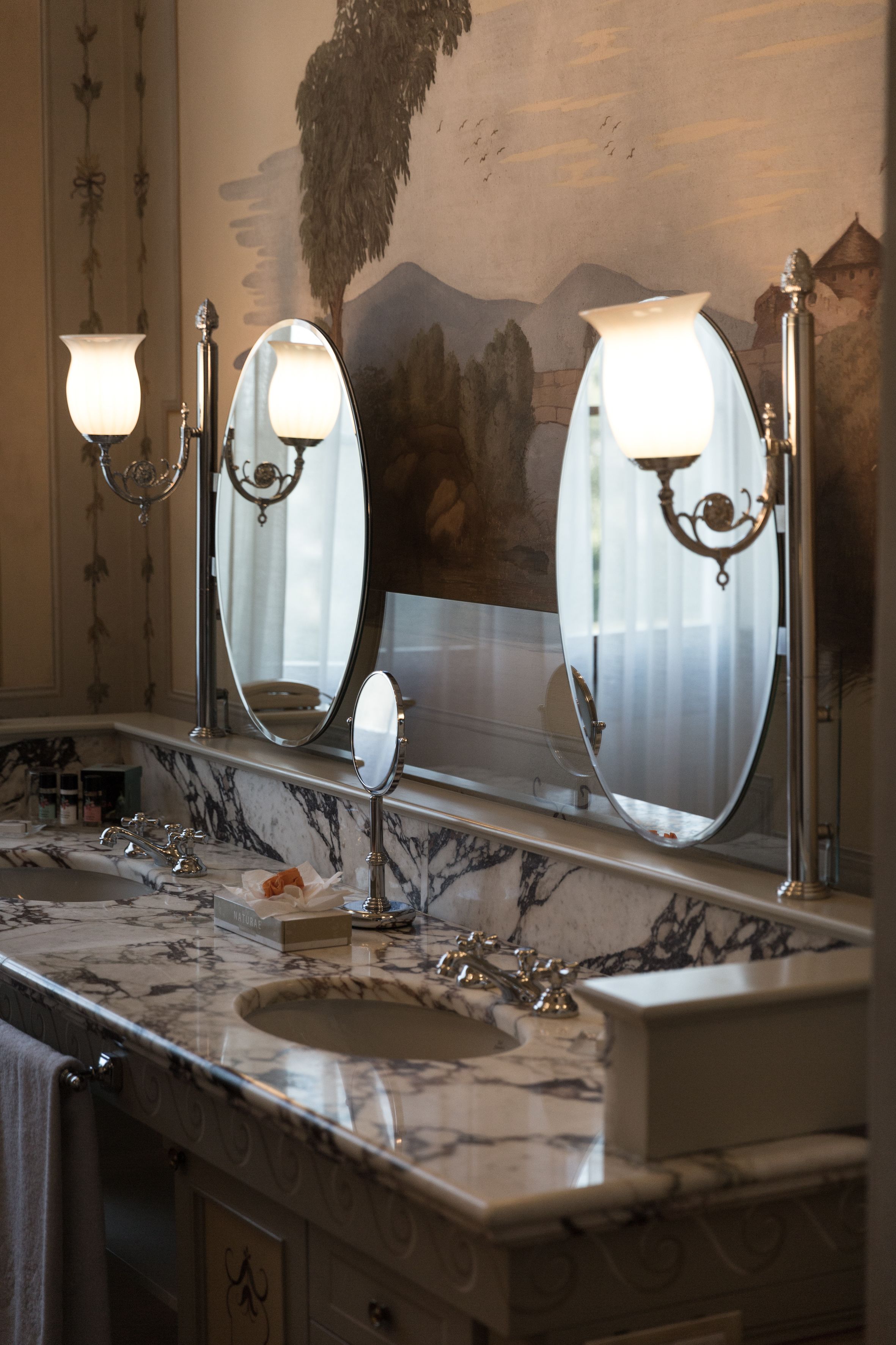 A bathroom with a marble sink, three wall-mounted mirrors, and a decorative mural.