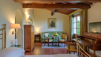 A hotel room with a bed, a wooden desk, a green sofa, a small table with flowers, and a painting on the wall.