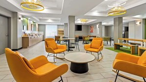 A modern hotel lobby with bright orange chairs, a central round table, and contemporary lighting fixtures. - Spark by Hilton Catoosa (Catoosa)