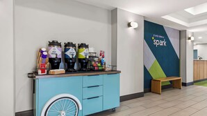 A blue cart with beverage dispensers and a wooden bench in a modern lobby. - Spark by Hilton Catoosa (Catoosa)