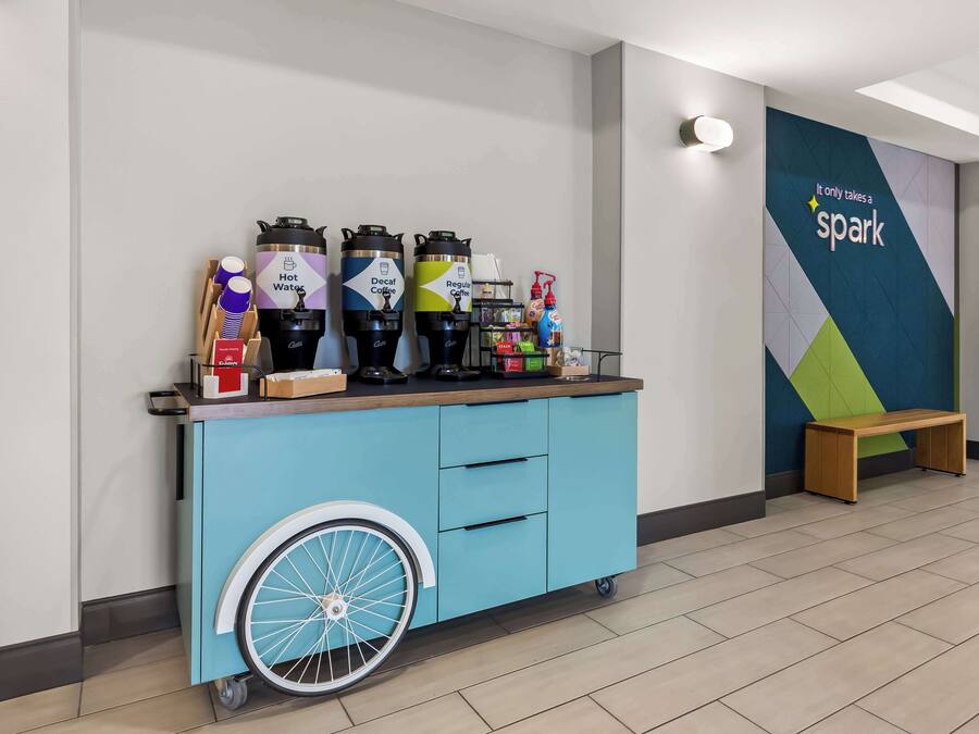 Een blauwe trolley met drankdispensers en een houten bankje in een moderne lobby.