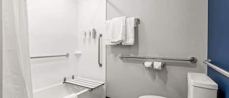 A modern bathroom with a bathtub, toilet, and handrails.