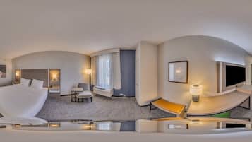 A modern hotel room with a curved ceiling, a large bed, a seating area with a table and chairs, a TV, and a window with curtains.
