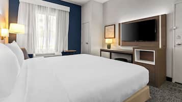 A hotel room with a large bed, a desk with a flat-screen TV, a window with curtains, and a door.