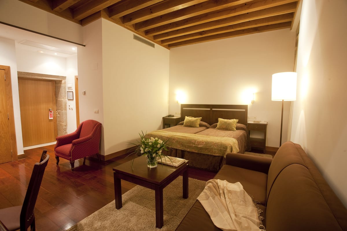 Ein Hotelzimmer mit einem Bett, einem Nachttisch, einem roten Sessel, einem Holztisch und einer braunen Couch.