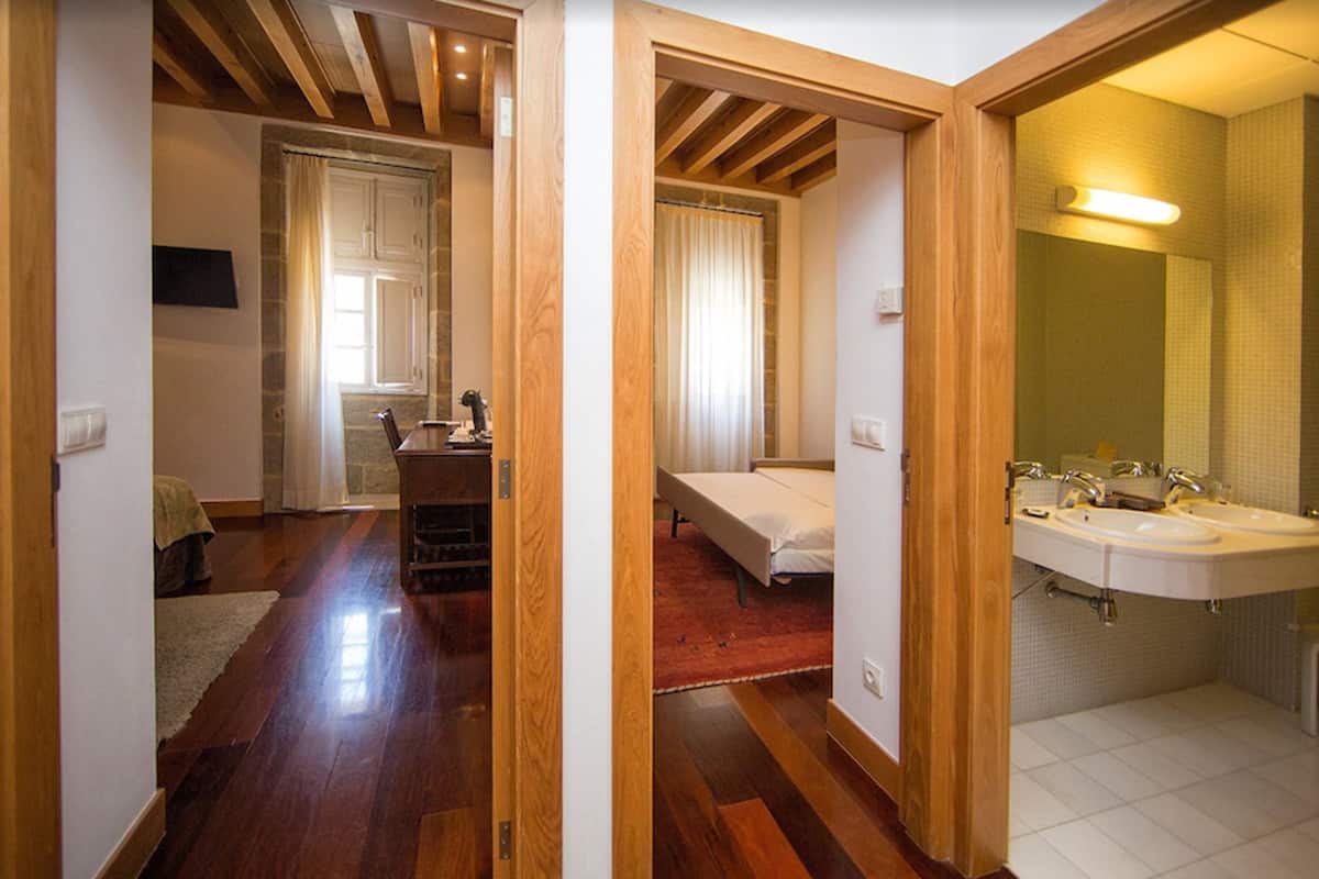 Ein Zimmer mit Holzböden, einem Bett, einem Schreibtisch und einem Badezimmer mit Waschbecken und Spiegel.